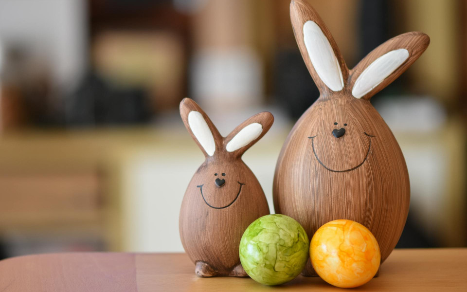Two wooden rabbits standing on a table behind colorful Easter eggs.