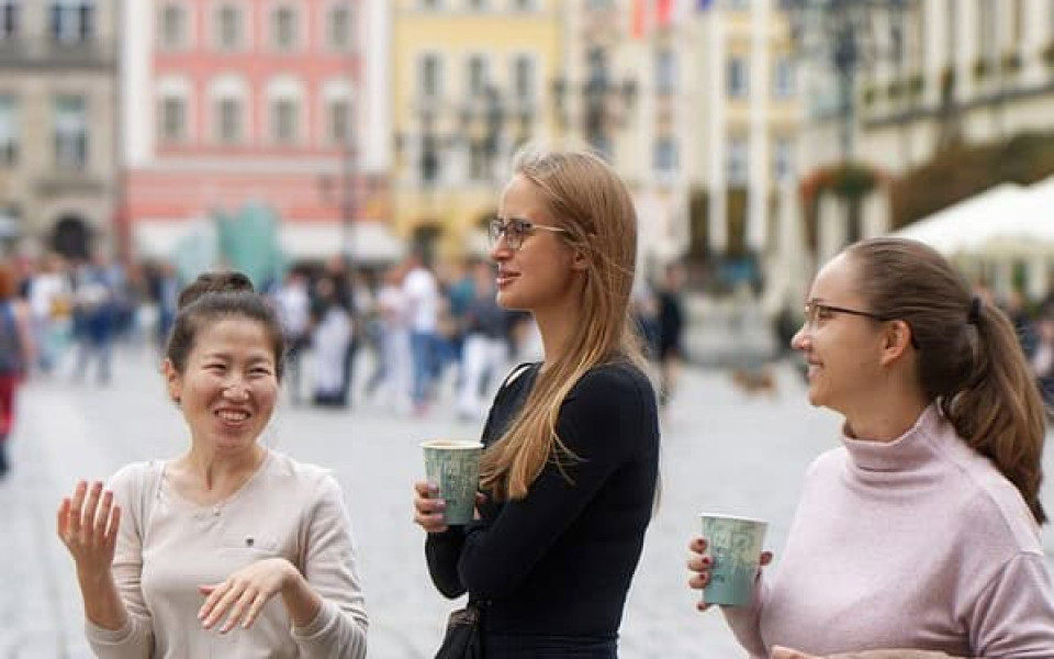 Some people carrying to go cups of coffee stand together in a city square.