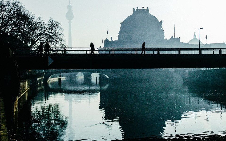 The outline of the Berlin skyline with its reflection in water running under a bridge.