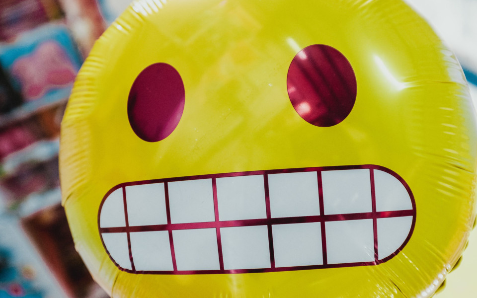 A inflated, round foil balloon with of the cringing face emoji.
