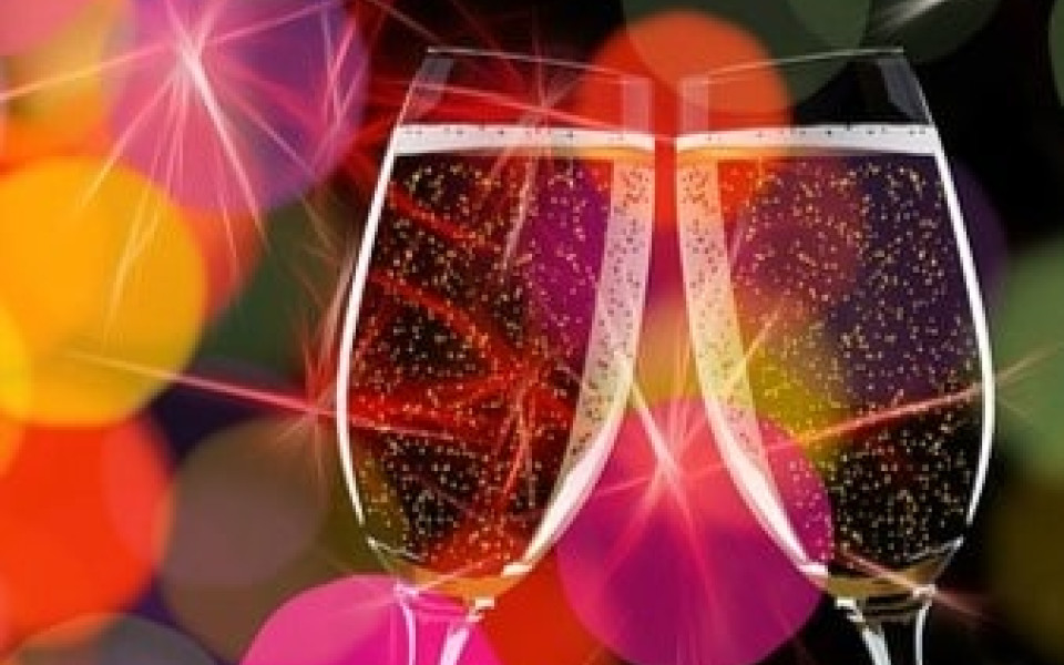 Two glasses on sparkling wine coming togerher in a toast in front of a festive background.