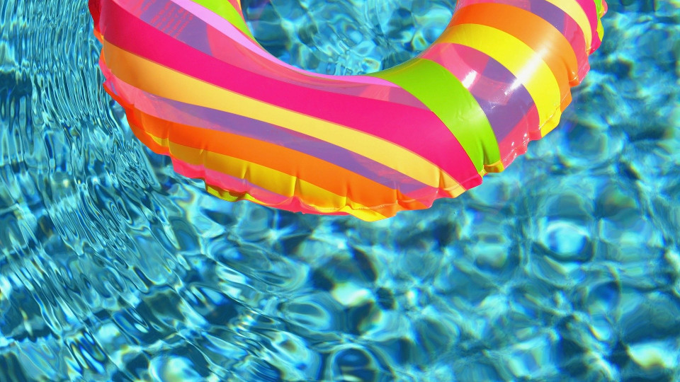 A colorful inflatable pool ring floats in clear, sunlit water.