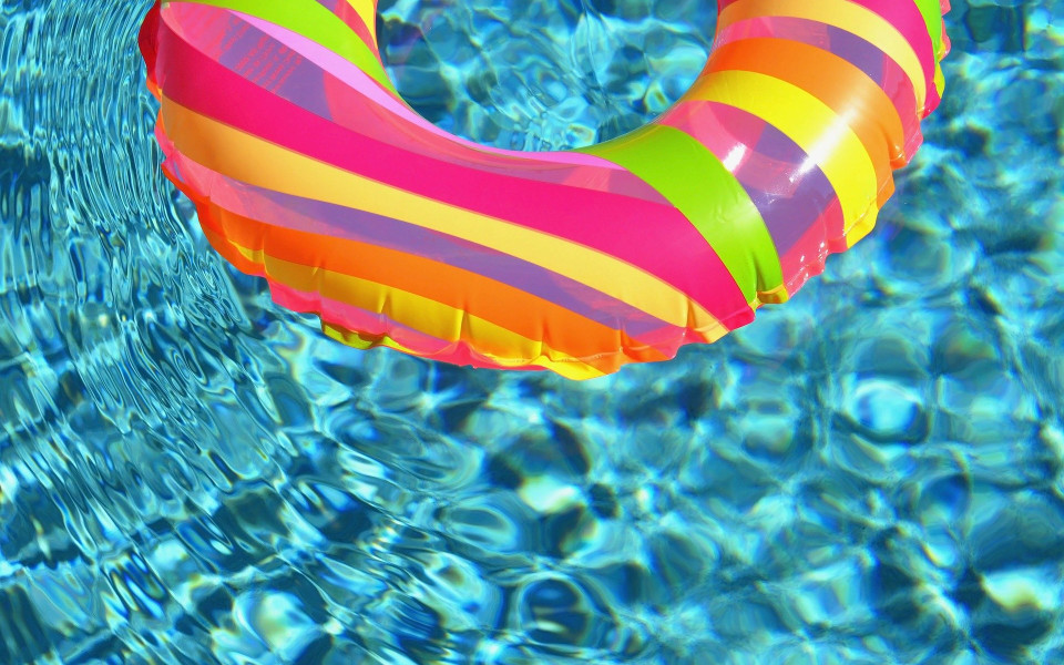 A colorful inflatable pool ring floats in clear, sunlit water.